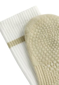 Witte geribbelde sokken met een beige antisliptextuur op de zool. De beige sok heeft een stippenpatroon en subtiele branding.