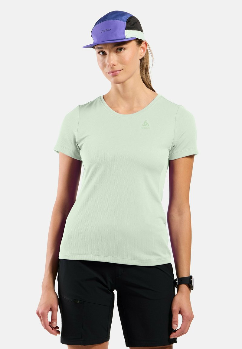 Light green short-sleeve T-shirt with a textured finish and small logo on the chest, paired with black shorts and a multicolored cap.