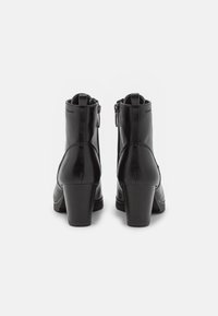 Bottes noires à la cheville avec une finition en cuir brillant, bout rond, talon bloc de hauteur moyenne et zips latéraux pour un enfilage facile. Texture lisse et décorations minimales.