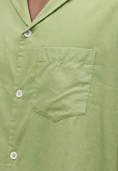 Ανοιχτοπράσινο πουκάμισο με κουμπιά και μία τσέπη στο στήθος, με λευκά κουμπιά, δείχνει το γιακά και την πάνω περιοχή του στήθους.