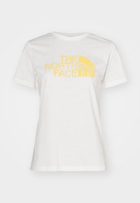 Camiseta de algodón blanca con un estampado gráfico amarillo de "THE NORTH FACE" y un logotipo en arco, con mangas cortas y cuello redondo.