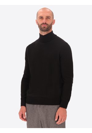 Maglione nero a collo alto realizzato in tessuto morbido. Design aderente con maniche lunghe e polsini e orlo a coste. Indossato con pantaloni grigi.