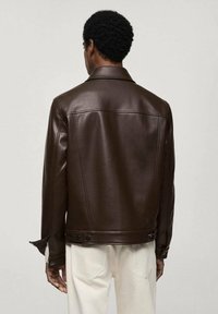 Veste en cuir synthétique marron avec un col pointu, des détails de motif et des manches à boutons. Elle présente une texture lisse et une coupe ajustée.
