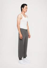Grå joggebukser med snøring, løs passform, laget av bomullsblanding, kombinert med en hvit tanktop og hvite joggesko. Enkel, minimalistisk design.