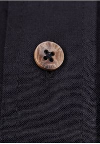 Sort stof med en tekstureret vævning, prydet med en rund træknap med et udskåret design med fire huller og ordet "HONESTY" indgraveret.