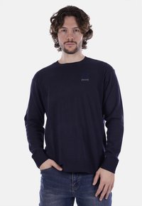 Maglione blu navy a maniche lunghe realizzato in morbido tessuto a maglia, con colletto e polsini a coste e un piccolo logo sul petto.