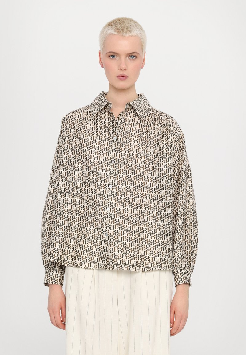Mønstret skjorte med krage, med et geometrisk design i beige og brun, lange ærmer og en løs passform. Kombinert med hvite stripete bukser.