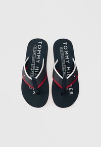 Navy sinised plätud valgete ja punaste aktsentidega, millel on tekstuuriga rihm ja logoprintidega jalatallad. Paksud kummitaldad toe postikujundusega.