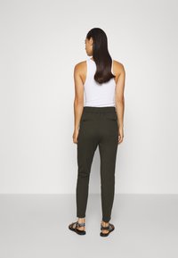 Donkergroene joggers met een slim fit, elastische tailleband en twee achterzakken; gecombineerd met een witte tanktop en zwarte sandalen.