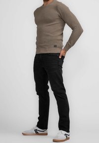 Beiger gerippter Pullover, runder Ausschnitt, lange Ärmel, kombiniert mit schwarzen Jeans und weißen Sneakers mit schwarzen und beigen Akzenten.