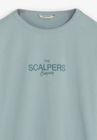 Camiseta de algodón azul claro con cuello redondo y mangas cortas. En la parte frontal aparece el texto "THE SCALPERS Company" en azul más oscuro.