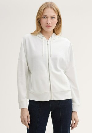 Sweat à capuche zippé blanc avec capuche, poignets et ourlet côtelés. Texture lisse avec cordons de serrage et poches latérales cachées. Design ajusté.