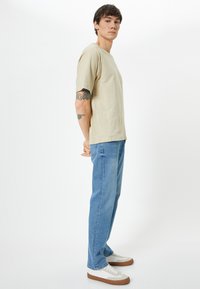 Camiseta de manga corta crema, con corte relajado, combinada con jeans rectos de color azul claro. Completada con zapatillas blancas con acentos marrones.