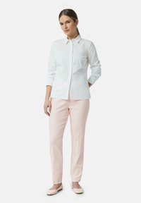 Camicia bianca a maniche lunghe, abbinata a pantaloni rosa chiaro su misura e scarpe basse chiare. Design semplice e pulito con una vestibilità classica.