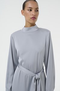 Robe élégante à manches longues en satin gris clair avec un col montant et un détail de ceinture nouée à la taille, dotée d'une texture lisse et d'un design minimaliste.