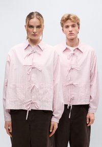 Ροζ, υφασμάτινα σακάκια με μακριά μανίκια και φιόγκους μπροστά καθώς και πλαϊνές τσέπες, συνδυασμένα με παντελόνια σκούρου καφέ χρώματος. Και οι δύο φορούν παρόμοια στυλ.