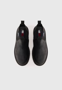 Par de botines negros sin cordones con punteras redondeadas y el logo de Tommy Jeans en las plantillas interiores y etiquetas laterales, fotografiados desde arriba.