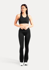 Musta urheiluliivit, joissa on pyöreä kaula-aukko ja racerback-malli, yhdistettynä korkeavyötäröisiin mustiin leggingseihin. Malli seisoo valkoisissa lenkkareissa.