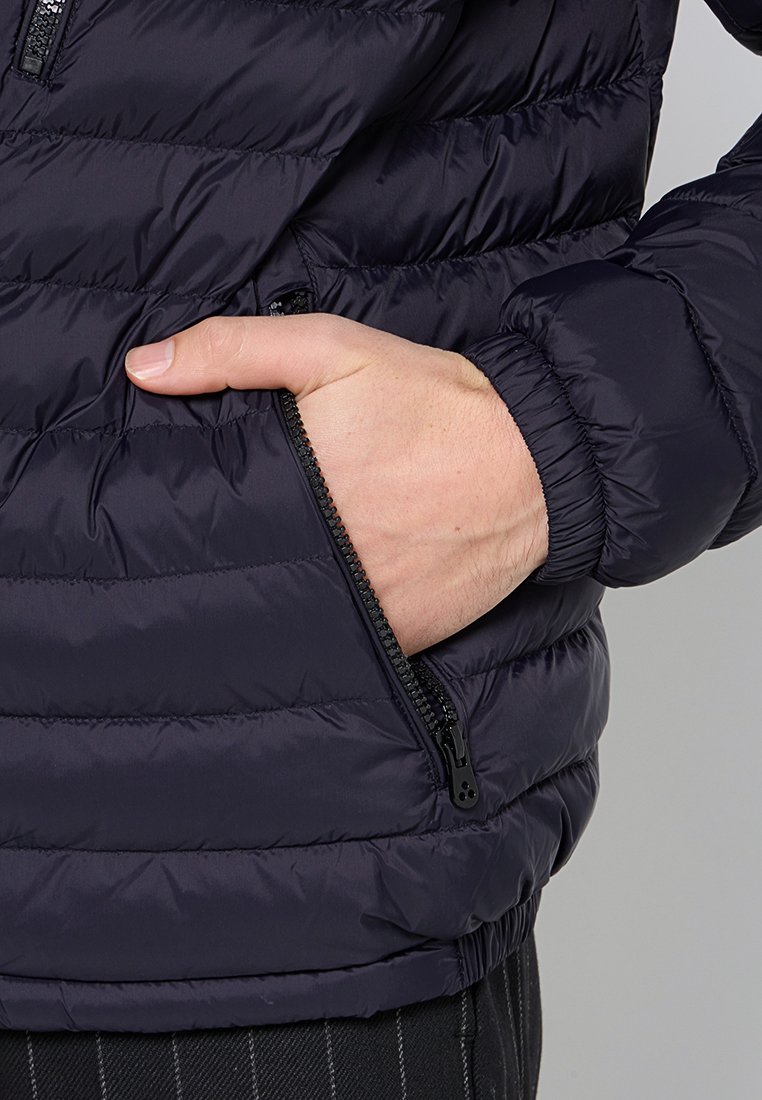 Giacca imbottita blu navy con design trapuntato, tasca con zip e polsini elastici. Tessuto leggero con una texture morbida.