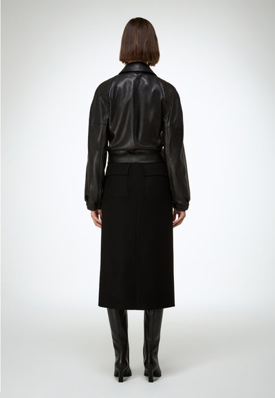 Crna kožna bomber jakna s pristajećim strukom, teksturiranim tkanjem, uparena s visokim crnim suknjom i čizmama od kože do koljena.