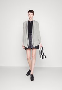 Cardigan gris clair avec des bords noirs, haut noir, jupe en cuir noire et sabots noirs. Tient un sac à carreaux noir et blanc.