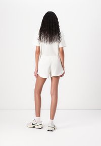 White ribbed two-piece outfit featuring a short-sleeve top and shorts, with a relaxed fit and rounded hems, paired with sneakers.