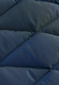 Dunkelblaues, gestepptes Gewebe mit einem Rautenmuster und einer glatten, glänzenden Textur sowie kontrastierenden Nähten entlang der Säume.