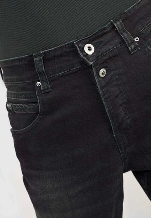 Jean en denim noir avec un design classique à cinq poches, des coutures visibles, une fermeture à bouton en métal et une légère décoloration de la texture du tissu.