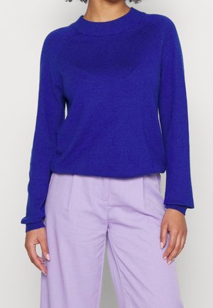 Blauwe crewneck trui van zachte gebreide stof, lange mouwen met geribbelde manchetten, gecombineerd met lichtpaarse broek. Soepele textuur met een relaxed fit.