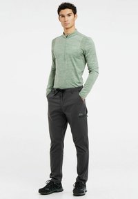 Lange mouwen, lichtgroene shirt met rits en donkergrijze broek met een verstelbare tailleband en zijrits pocket. Zwarte sneakers.