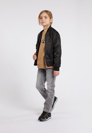 Veste bomber noire avec une texture à motif subtil, associée à un sweat-shirt marron et un jean gris slim. Baskets noires avec des accents orange.