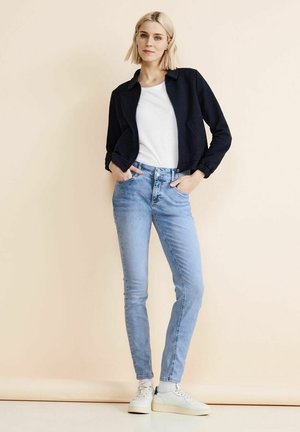 Navy zip-up jacket, white shirt, light blue skinny jeans, and white sneakers. Smooth textures with minimal accents and a fitted design.