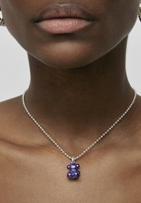 Collar de cadena de bola de plata con un colgante en forma de oso morado. El colgante tiene un acabado brillante con un cuerpo y orejas redondeadas.
