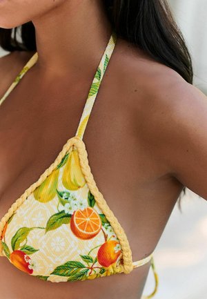 Prim-plan cu o femeie purtând un top de bikini galben cu model de fructe, cu desene de frunze portocalii și verzi, arătând gâtul și umărul.