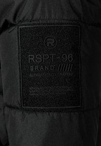 Crni platneni zakrpa s utisnutim natpisom: "RSPT-96 MARKA AUTENTIČNO IZRAĐENO." Teksture uključuju glatke i uzdignute elemente, s logotipom.