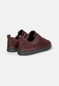 Sneaker in pelle bordeaux con punta arrotondata, suola piatta in gomma nera e dettagli di cucitura sottili. Presenta allacciatura frontale e un'impugnatura a forma di cappio sul tallone.