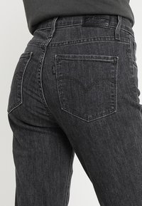 Jeans de mezclilla negros con una cintura alta, que cuentan con un diseño clásico de cinco bolsillos y costuras sutiles en los bolsillos traseros.