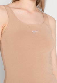 Ljusbrun linne i mjukt, elastiskt material med rund halsringning och slim fit, som har en liten vit Nike-logotyp på bröstet.