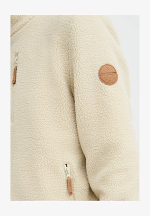 Krémový fleecový pulóver s textúrovaným povrchom. Obsahuje polovičný zips a koženú nášivku na rukáve. Zipsové detaily sú v bielej farbe.