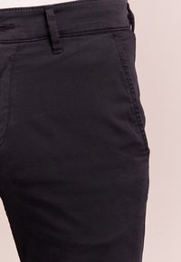 Pantalon en coton noir avec une coupe ajustée, des passants pour ceinture, et une texture lisse avec des détails de couture minimalistes.