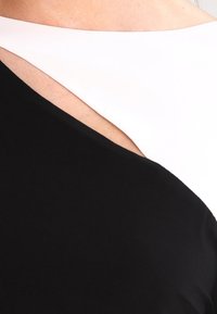 Svart och vit klänning med ett diagonalt färgblockeringsdesign och en slät textur, som avslöjar en utskärning närmast halsringen.