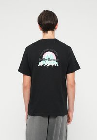 T-shirt preta de algodão com um gráfico colorido de montanha e texto nas costas, com detalhes "Helly-Hansen" e "Proteção Profissional".