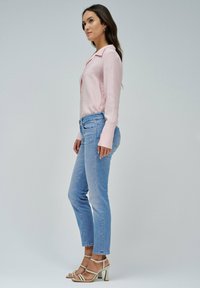 Camisa de botones rosa de mangas largas, vaqueros azul claro con corte recto y sandalias de tacón beige. Diseño sencillo sin patrones.