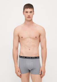 Boxeri din bumbac gri, cu talie neagră, având inscripția albă "PIER ONE". Design ajustat și textură netedă. Modelul este prezentat fără cămașă.