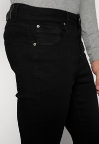 Svarta jeans i denim, med slim fit, fem fickor och metallnitar. Tygkvaliteten är slät och ogenomskinlig.