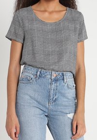 Sort-hvid ternet kortærmet top med rund halsudskæring, sammen med lys blå højtaljede slidte jeans. Flad stoftekstur.
