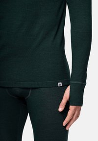 Dunkelgrünes Thermooberteil mit langen �Ärmeln, glatter Textur und einem kleinen Logopatch am Saum, kombiniert mit passenden Hosen.