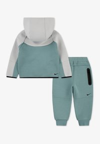 Hoodie de sport en teal clair et joggers assortis. Le hoodie a une capuche grise, des panneaux de manches contrastants et des accents noirs. Les joggers possèdent une poche zippée.