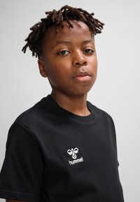 Camiseta negra de algodón con escote redondo, presenta un logo bordado en blanco en el lado izquierdo del pecho. Tejido texturizado, mangas cortas.