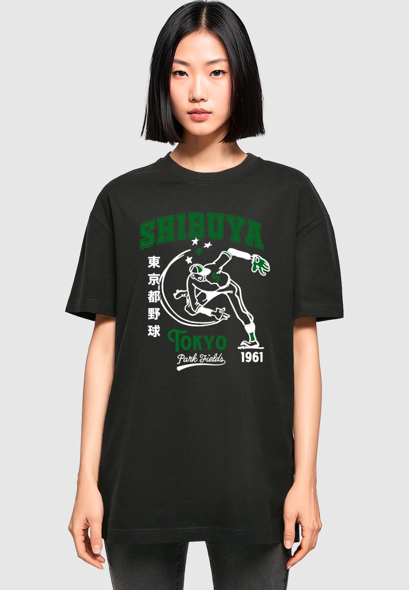 Sort bomulds T-shirt med et stort grafisk print med "SHIBUYA" i grøn og hvid, som viser en skater og tekstdetaljer, afslappet pasform.